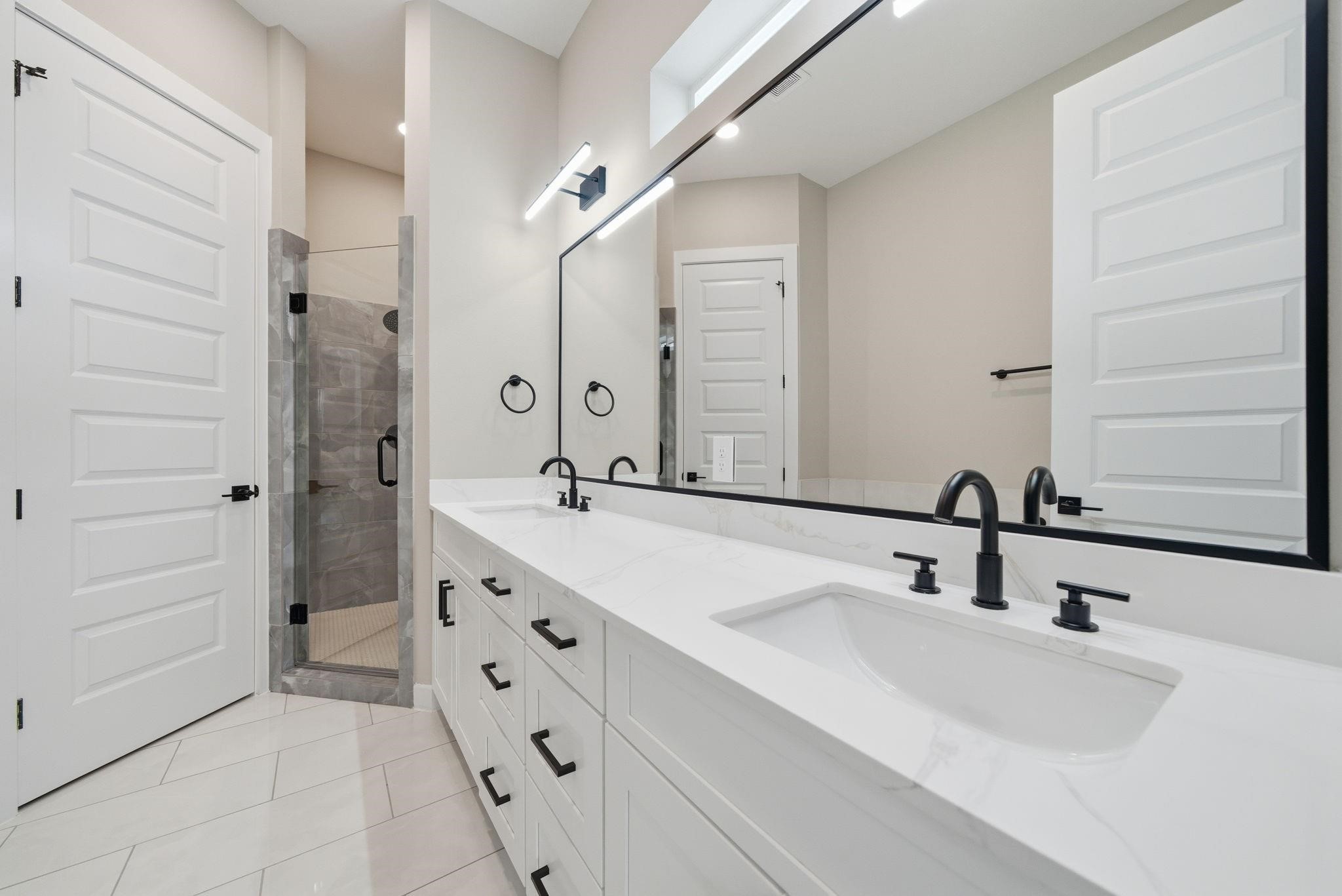 4013 Griggs Road, Unit F Houston, TX 77021 - Photo 8 of 35 Elegant bathroom featuring a spacious dual-sink vanity with modern black fixtures, a large mirror, and a stylish glass-enclosed shower.