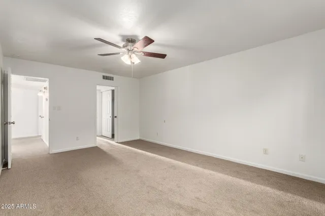 an empty room with chandelier fan and windows