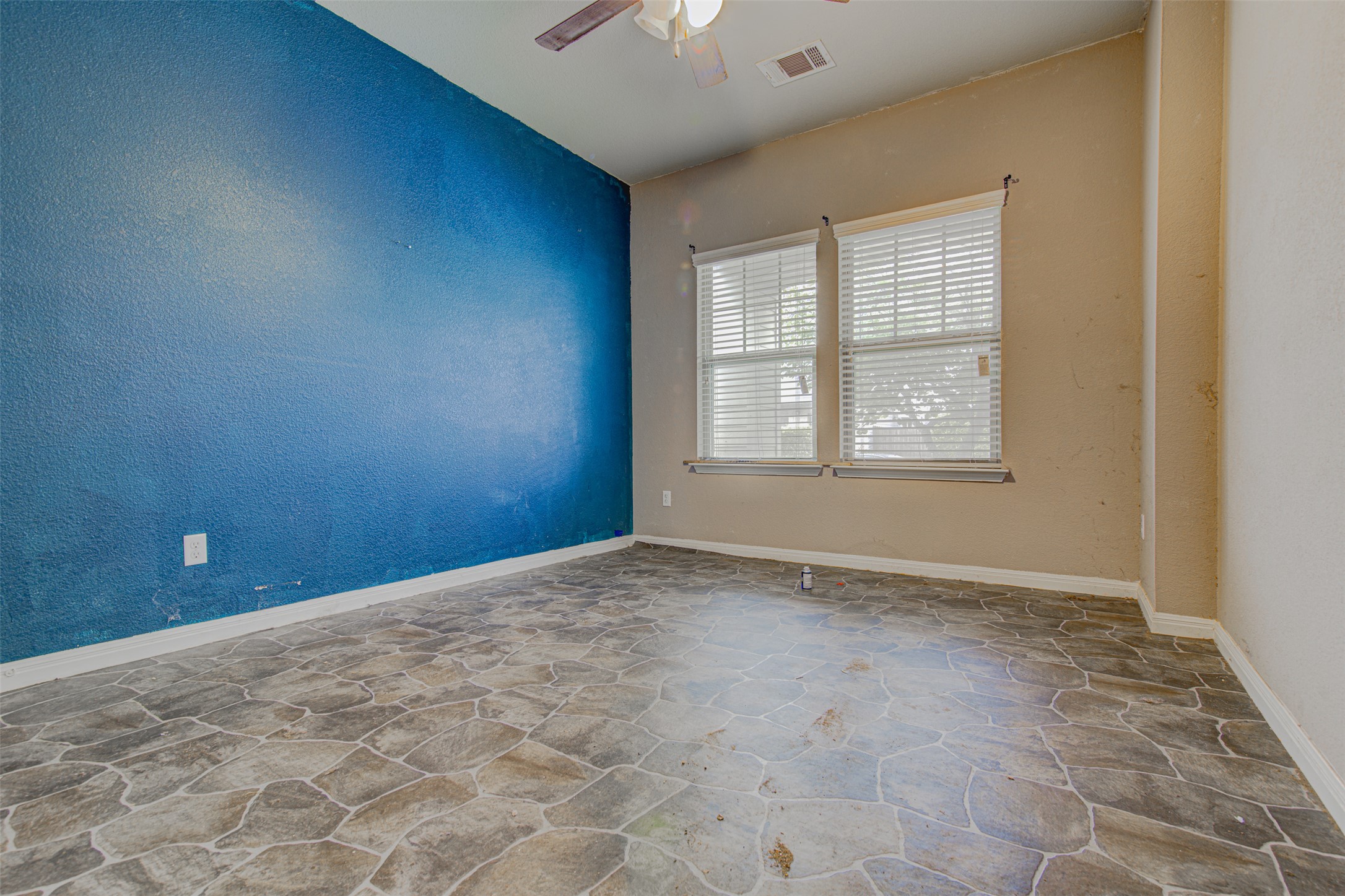 4527 Kind Way, Unit 231 Austin, TX 78725 - Photo 8 of 18 Interior room featuring patterned stone-look flooring, a blue accent wall, two windows with blinds, a ceiling fan, and sloped ceilings