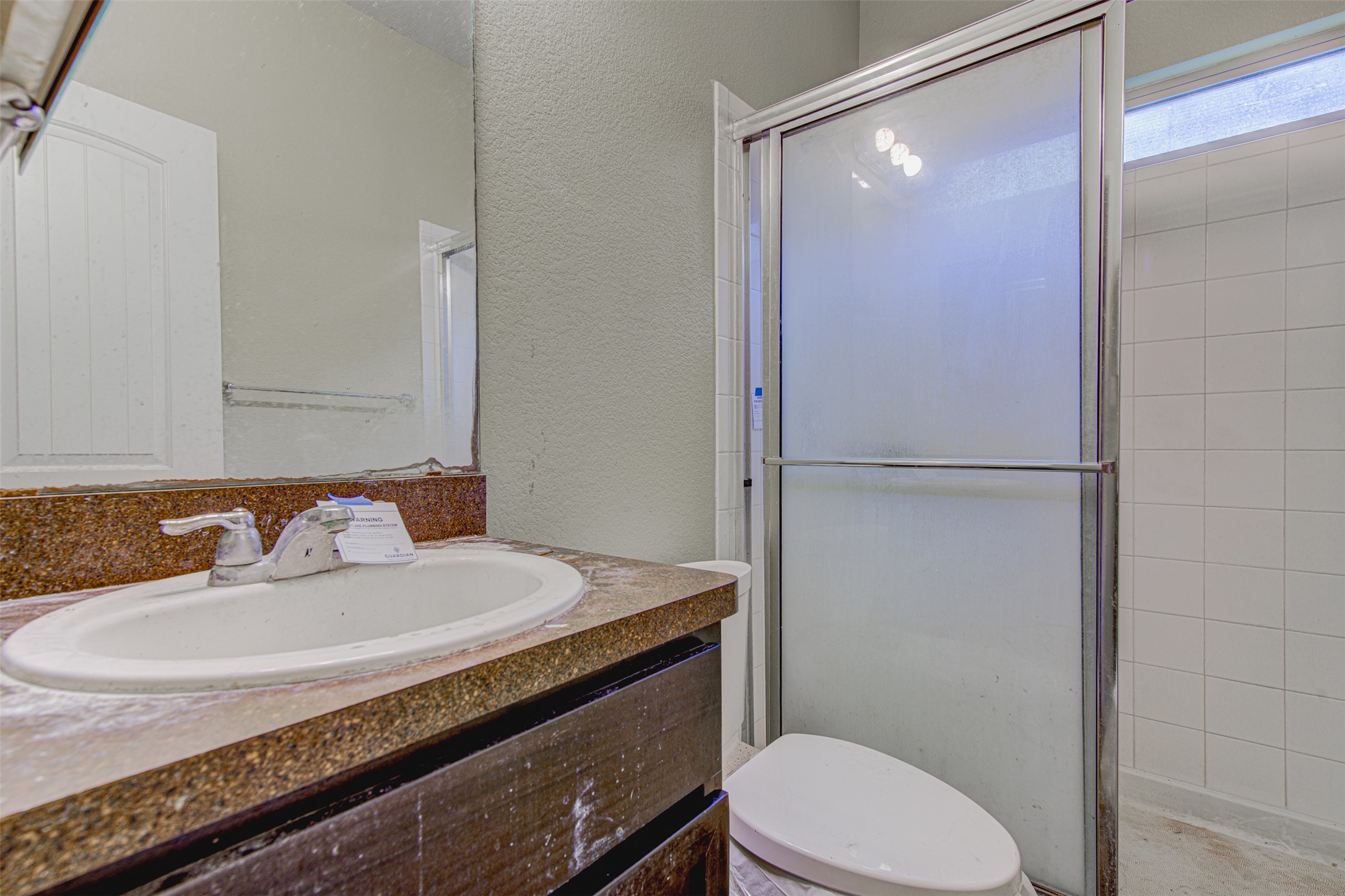 4527 Kind Way, Unit 231 Austin, TX 78725 - Photo 9 of 18 Bathroom featuring an integrated vanity sink with a speckled countertop, dark wood-finish cabinetry, and a shower enclosure with frosted glass panels and a chrome frame