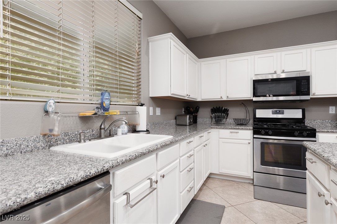 99 Milicity Road Henderson, NV 89012 - Photo 12 of 51 Kitchen with appliances with stainless steel finishes, white cabinets, light tile patterned floors, and light stone counters