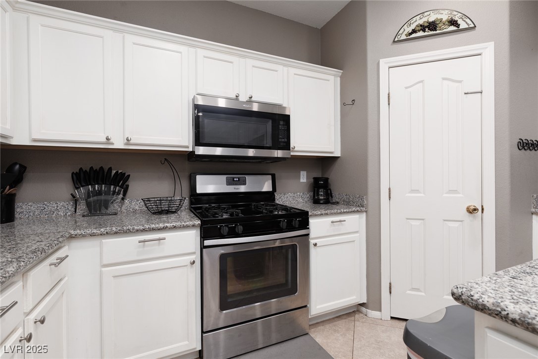 99 Milicity Road Henderson, NV 89012 - Photo 13 of 51 Kitchen featuring stainless steel appliances, white cabinets, light tile patterned floors, and light stone countertops
