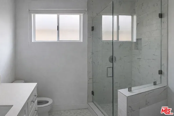 a bathroom with a granite countertop toilet a sink a window and shower