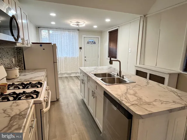 a kitchen with granite countertop a refrigerator a sink dishwasher and a stove with wooden floor