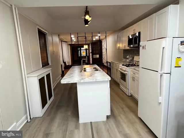 a kitchen with stainless steel appliances kitchen island a white stove top oven a sink dishwasher and white cabinets with wooden floor