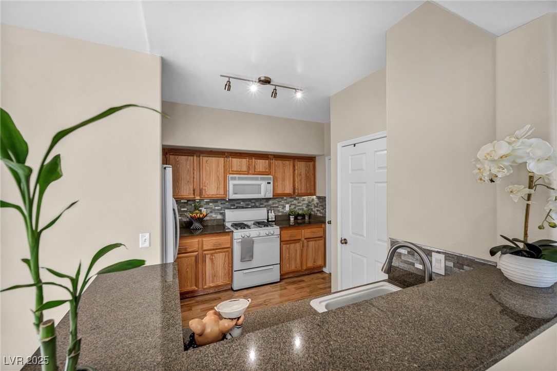 10550 West Alexander Road, Unit 2103 Las Vegas, NV 89129 - Photo 16 of 45 Kitchen with a sink, tasteful backsplash, a peninsula, brown cabinets, and white appliances