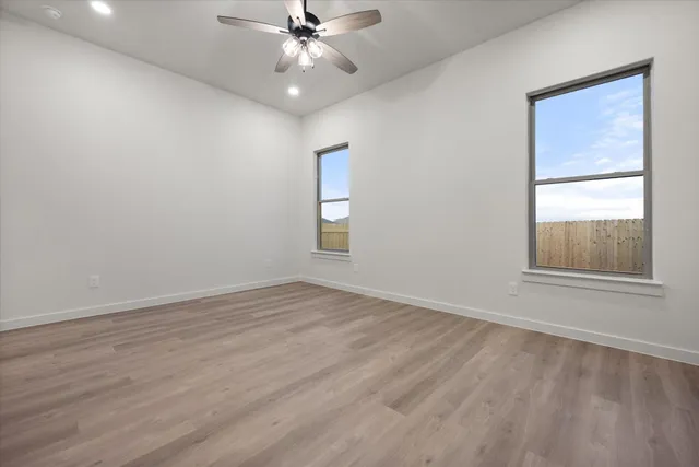 an empty room with wooden floor fan and windows