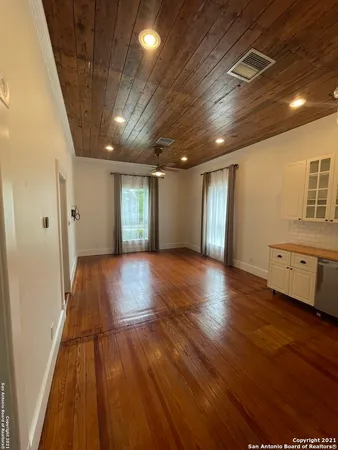 a view of an empty room with wooden floor and a kitchen