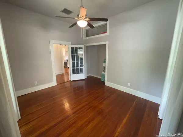 an empty room with wooden floor chandelier fan and windows