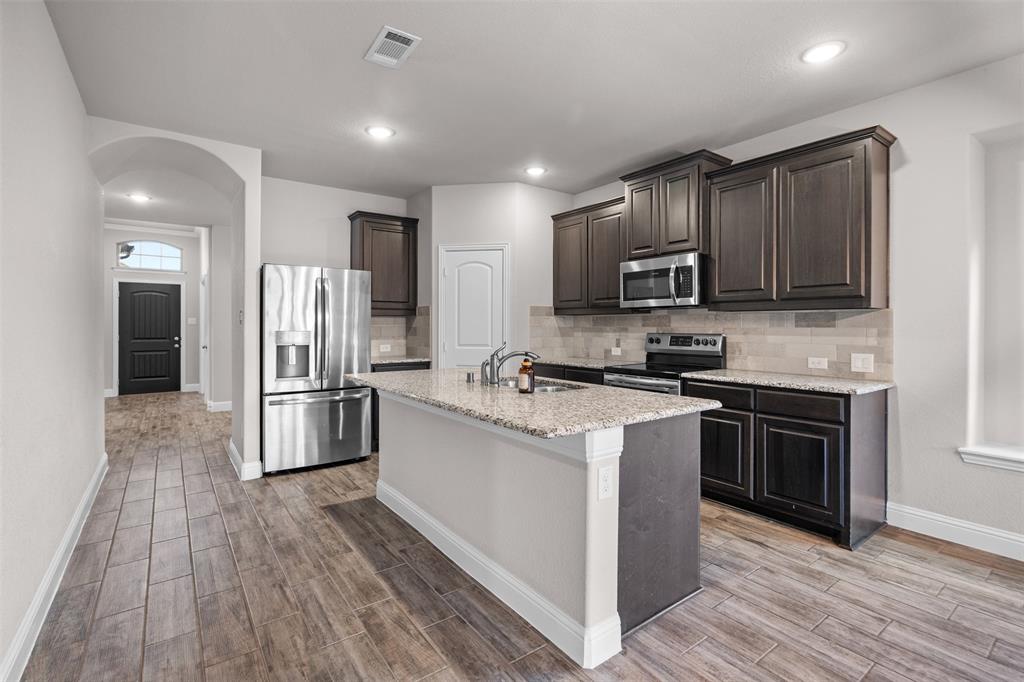 119 Happy Lane Red Oak, TX 75154 - Photo 12 of 37 Contemporary kitchen featuring a center island, dark wood cabinetry, stainless steel appliances, and tile flooring