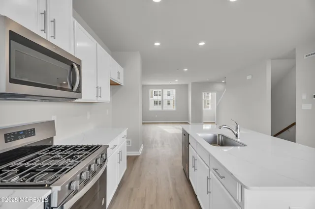 a kitchen with stainless steel appliances granite countertop a sink dishwasher a stove and a refrigerator with wooden floor