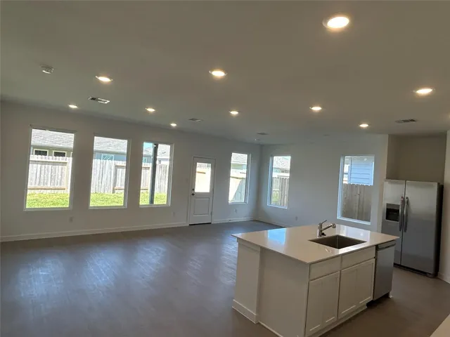 a living room with stainless steel appliances kitchen island granite countertop a refrigerator a sink a stove and a wooden floors