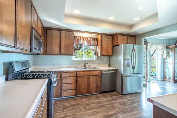 a kitchen with stainless steel appliances granite countertop a refrigerator a sink dishwasher a stove and white countertops with wooden floor