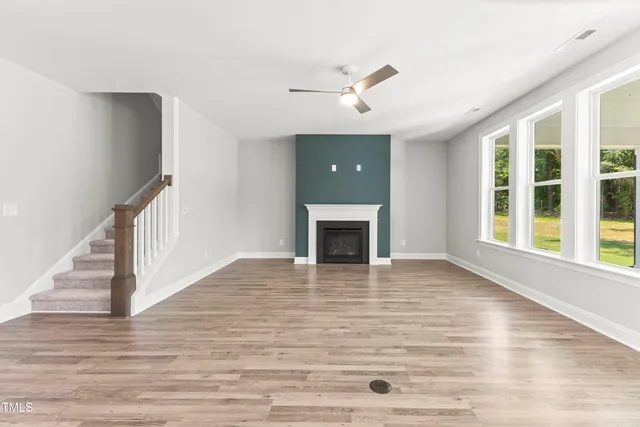 a view of an empty room with wooden floor fireplace and a window