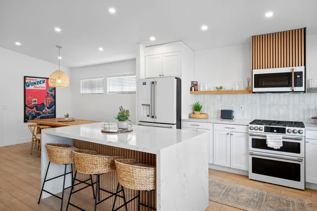 a kitchen with stainless steel appliances a stove a refrigerator a oven a sink a dining table and chairs with wooden floor