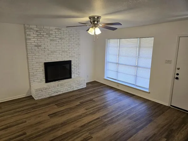 a view of an empty room with wooden floor fireplace and a window