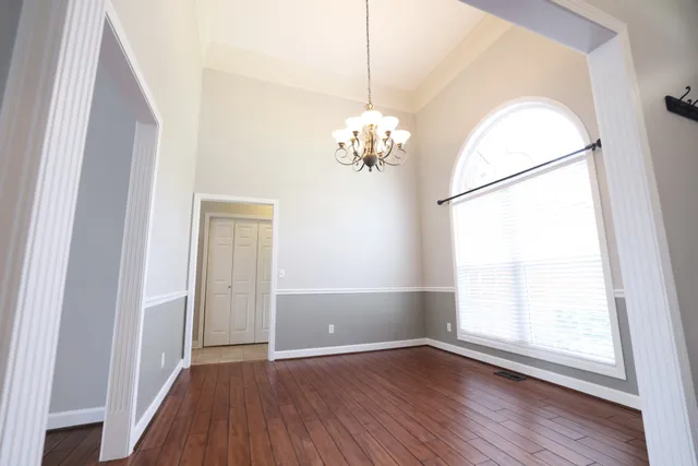 an empty room with wooden floor chandelier and windows