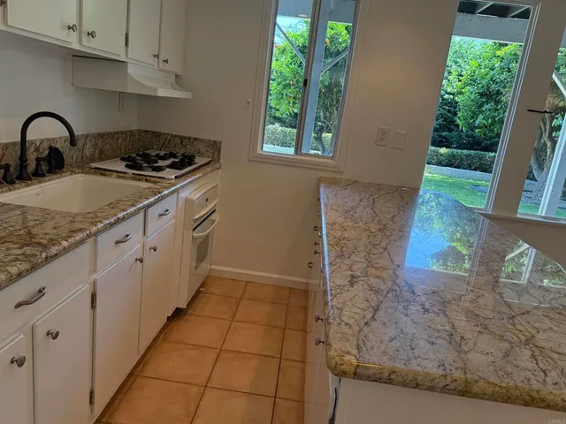 a kitchen with granite countertop a sink a stove a window and cabinetry