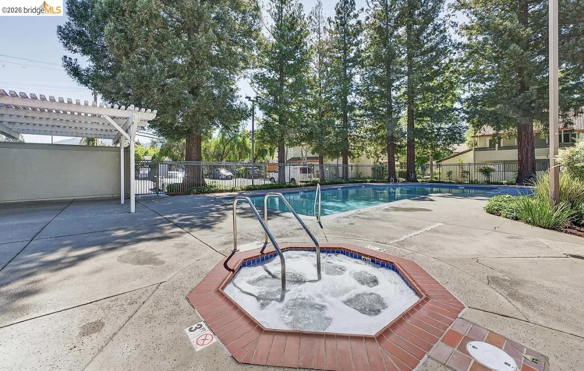 1505 Kirker Pass Road, Unit 214 Concord, CA 94521 - Photo 3 of 55 Outdoor spa with brick coping and adjacent swimming pool, surrounded by concrete decking, a white pergola, and mature trees