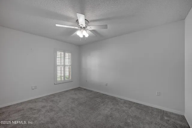 an empty room with chandelier fan and windows