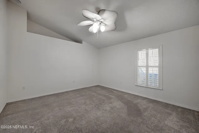 an empty room with chandelier fan and windows