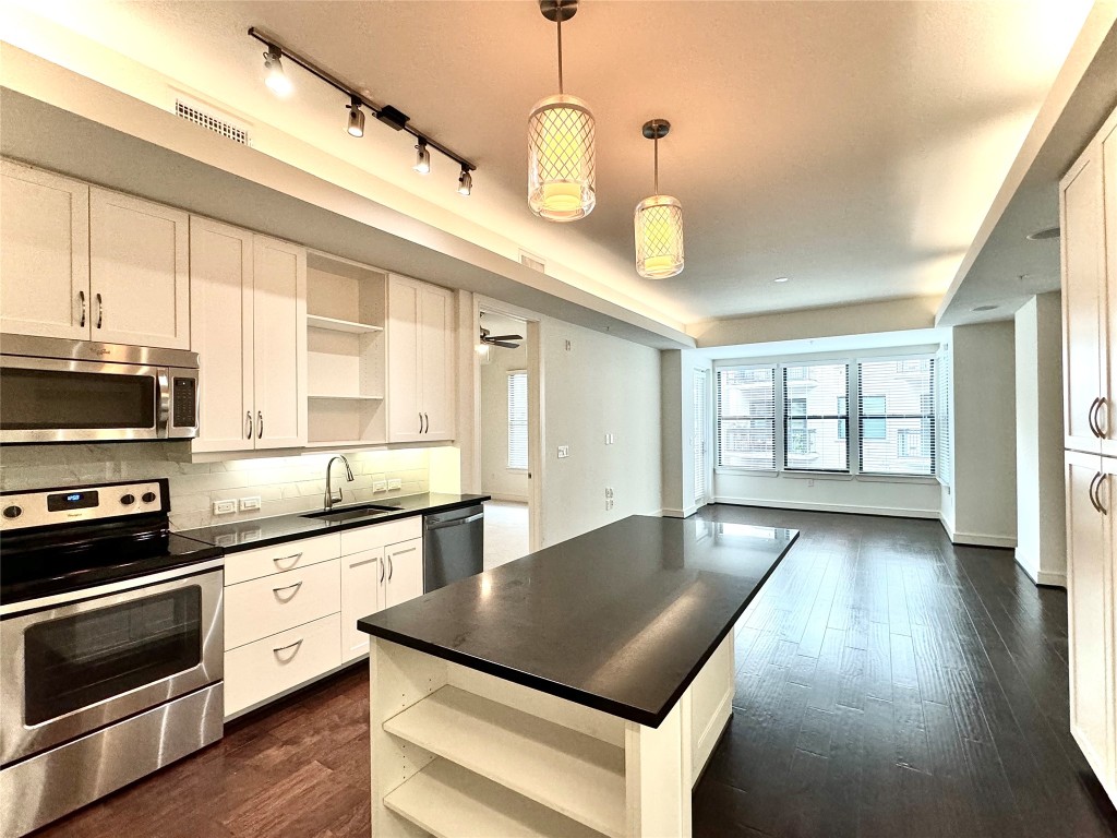 a kitchen with stainless steel appliances granite countertop a stove a sink and white cabinets with wooden floor