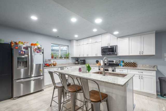 262 North Santa Fe Drive Mapleton, UT 84664 - Photo 21 of 28 Kitchen with light stone countertops, stainless steel appliances, white cabinets, a breakfast bar area, and a center island with sink