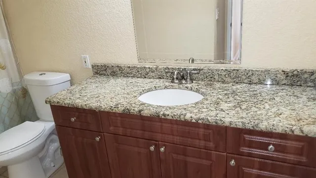 a bathroom with a granite countertop sink and a toilet