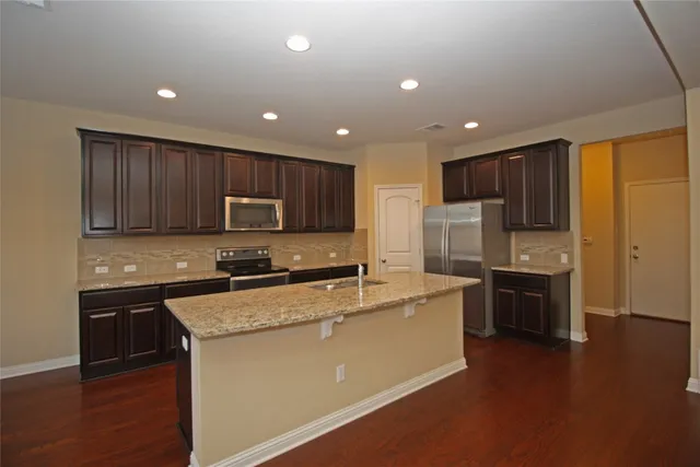 a kitchen with stainless steel appliances granite countertop a refrigerator a stove top oven a sink and dishwasher with wooden floor