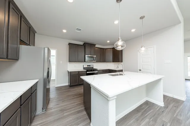 a large kitchen with kitchen island a sink dishwasher a stove a refrigerator and white cabinets with wooden floor