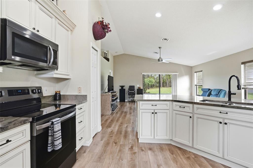 11437 Deercroft Court Spring Hill, FL 34609 - Photo 11 of 37 a kitchen with white cabinets a sink dishwasher and a stove with wooden floor