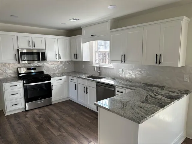 a kitchen with stainless steel appliances granite countertop a sink dishwasher stove and white cabinets with wooden floor