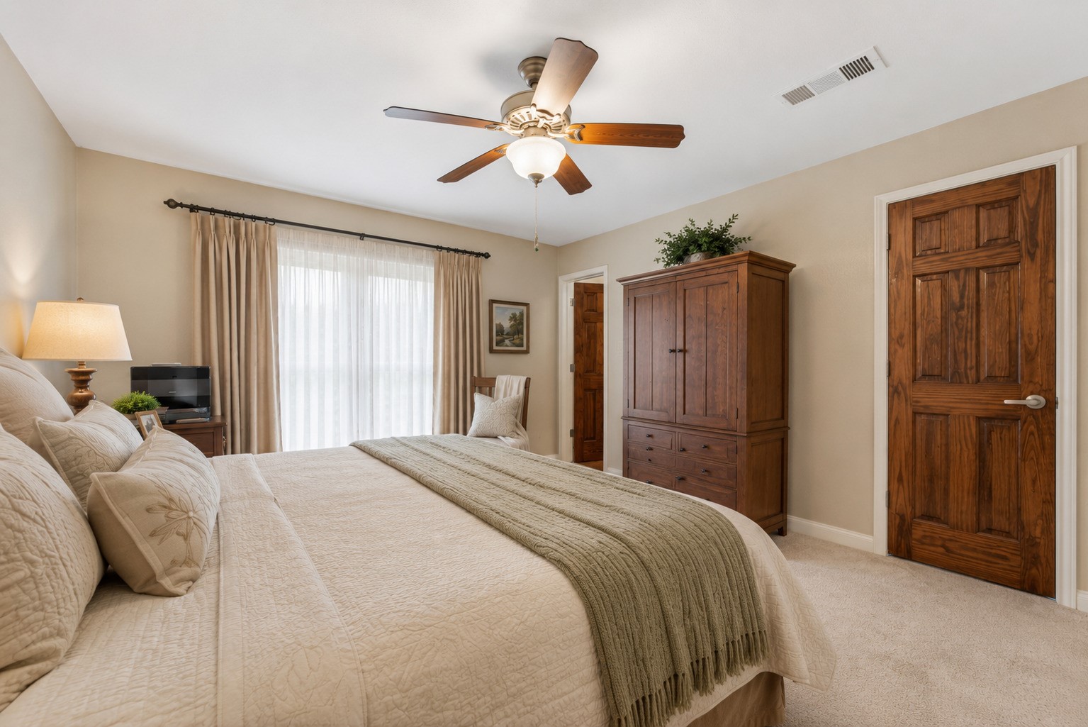 1004 Wagon Road Simonton, TX 77485 - Photo 18 of 40 From this angle, the primary bedroom's spacious and versatile layout is on full display, custom solid wood door, with plush carpeting and a ceiling fan adding to the room's comfort. A large window allows natural light to flow in, while a rich wood panel door leads to the en suite bathroom, adding both privacy and convenience.