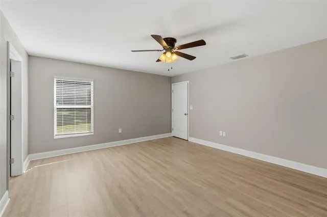 an empty room with wooden floor ceiling fan and windows
