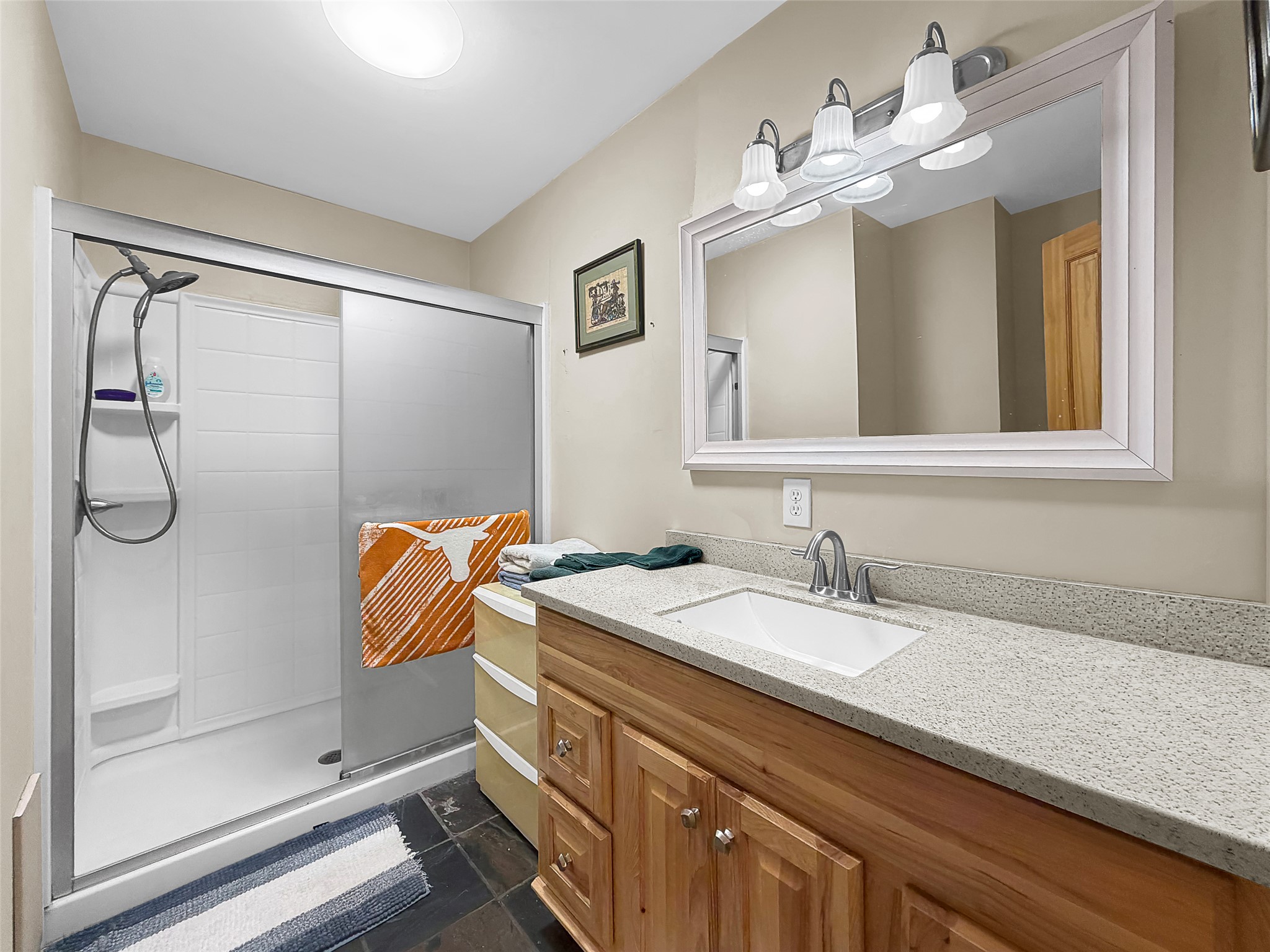 925 Long Hollow Road Dale, TX 78616 - Photo 11 of 26 Bathroom featuring a walk-in shower with sliding frosted glass doors, a vanity with a light-toned countertop, a rectangular undermount sink, a chrome faucet, and a large framed mirror with overhead vanity lighting
