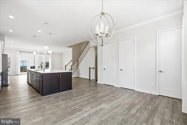 a living room with couches chandelier and kitchen view with wooden floor