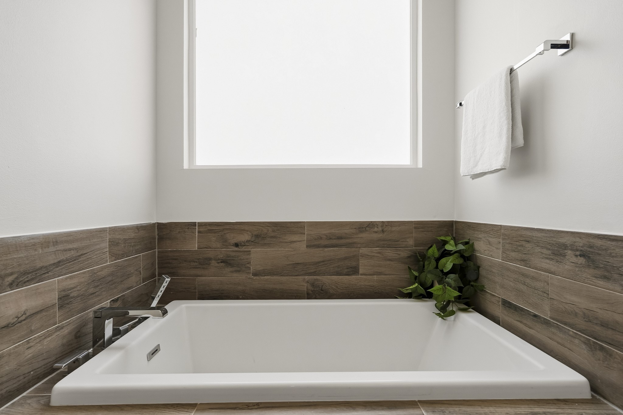 2004 Rosedale Street, Unit D Houston, TX 77004 - Photo 27 of 45 The luxurious soaking tub commands attention as a striking focal point, wrapped in hardwood-like tile for a rich, custom finish. An obscure frosted-glass window above softly filters natural light while preserving privacy, enhancing the bath’s serene, spa-inspired atmosphere.