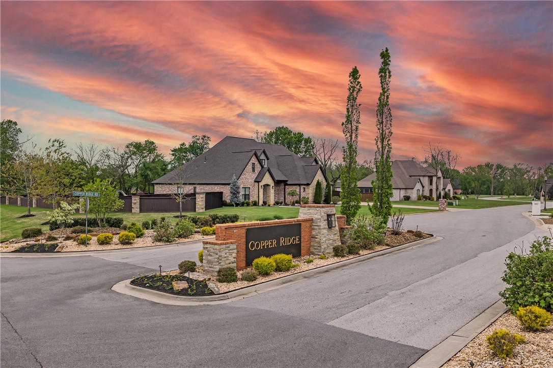 3510 Copper Ridge Road Rogers, AR 72756 - Photo 23 of 58 The property is located within a community featuring a welcoming stone and brick entrance sign, surrounded by paved roads and well-maintained landscaping with various shrubs and trees