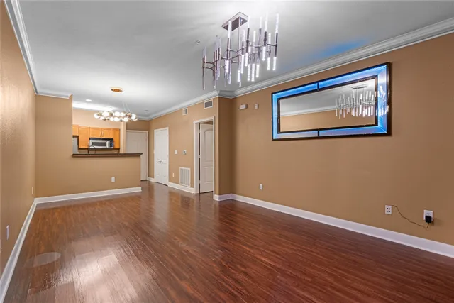 a view of an empty room with wooden floor and a kitchen