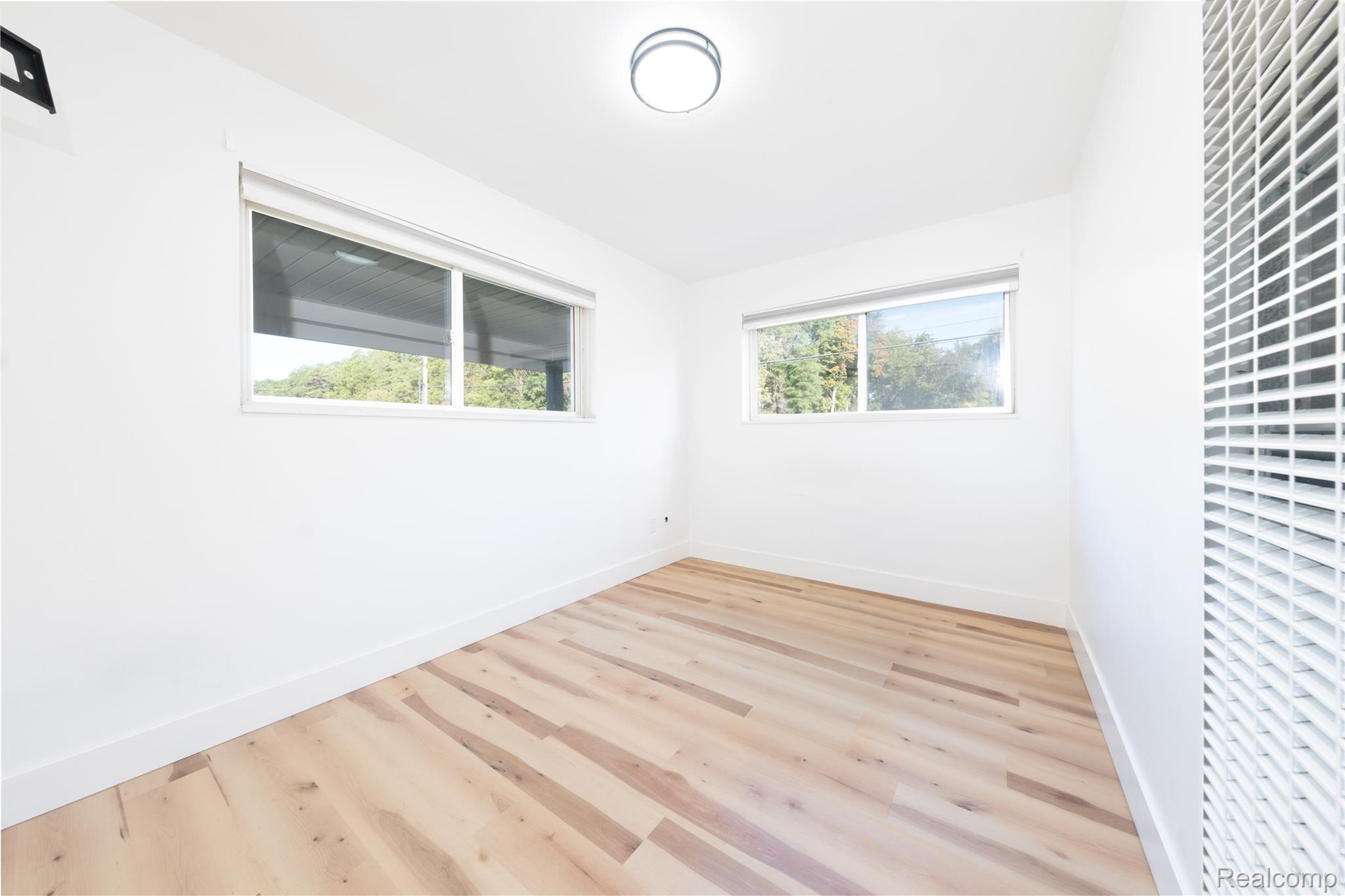 3065 South Commerce Road, Unit 9 Walled Lake, MI 48390 - Photo 10 of 15 White walls with wood-finish flooring, two windows, and a flush mount ceiling light