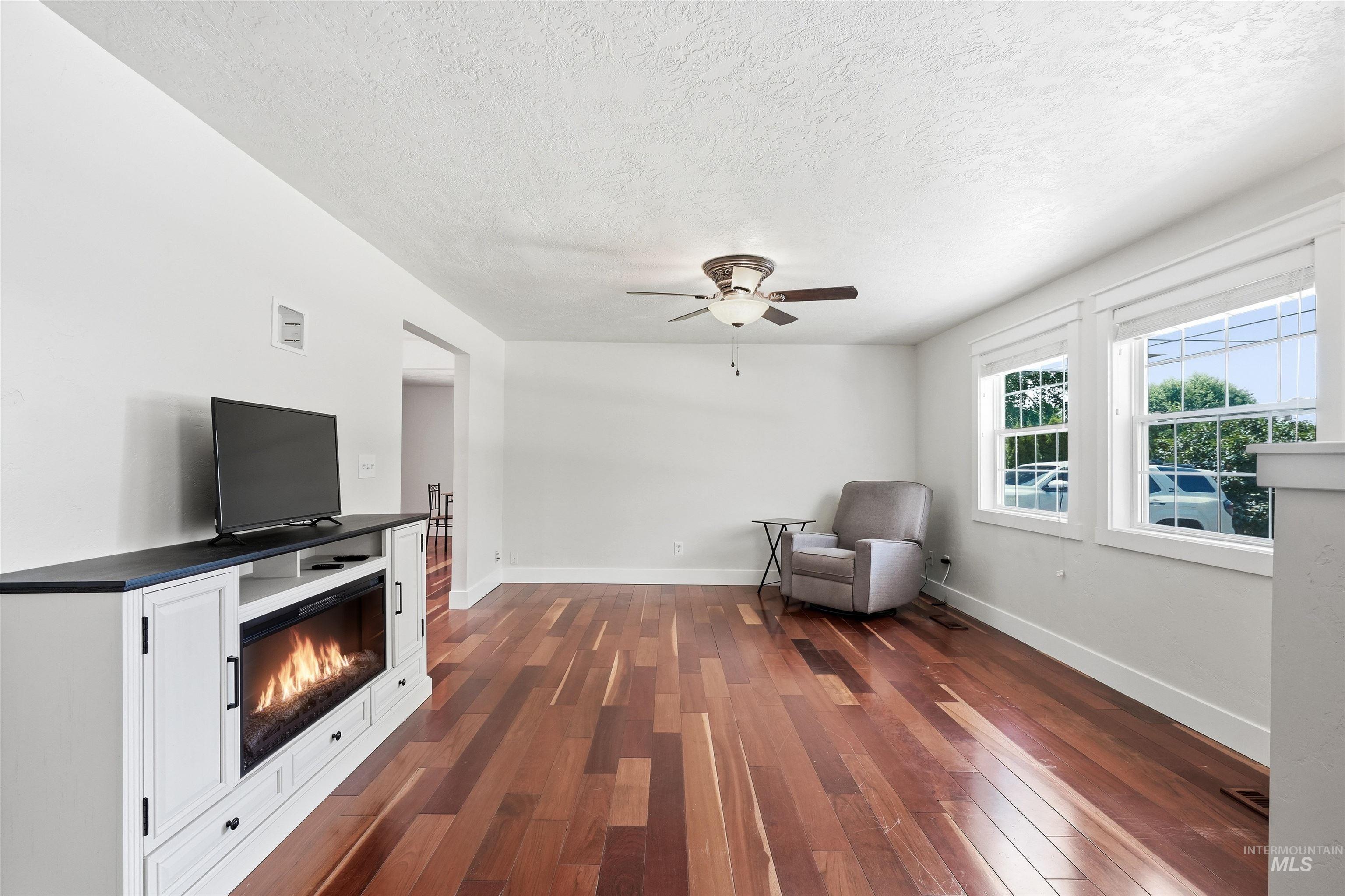 23650 Freezeout Road Caldwell, ID 83607 - Photo 5 of 42 Bright interior space featuring rich wood-finish flooring, a white built-in entertainment console with an electric fireplace, a ceiling fan, and multiple windows providing natural light