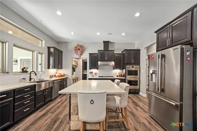 a kitchen with stainless steel appliances granite countertop a refrigerator a sink dishwasher a stove and white cabinets with wooden floor