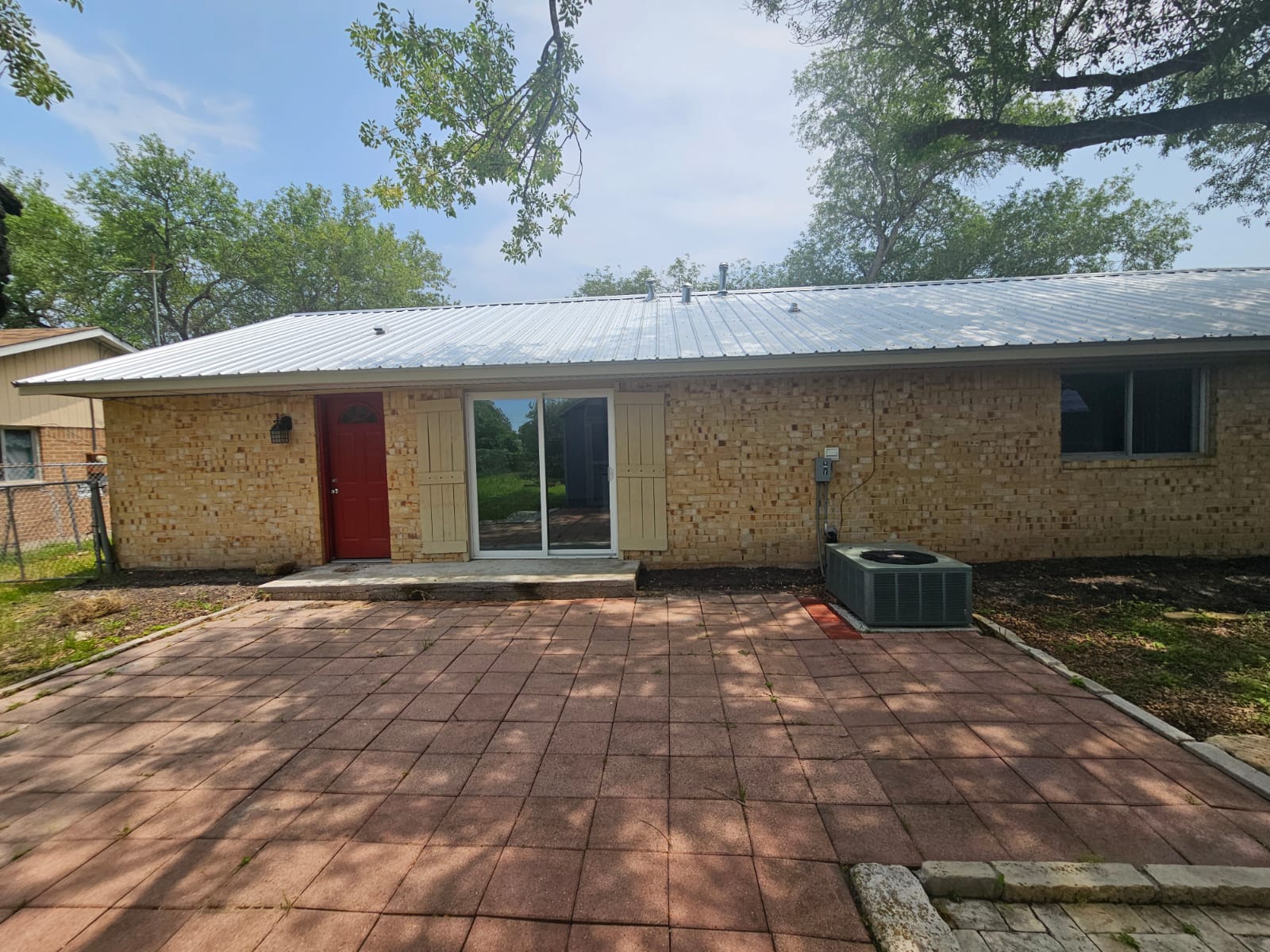 1401 Trinity Street Lockhart, TX 78644 - Photo 26 of 31 Brick exterior featuring a metal roof, red entry door, sliding glass door, and an exterior patio with square pavers