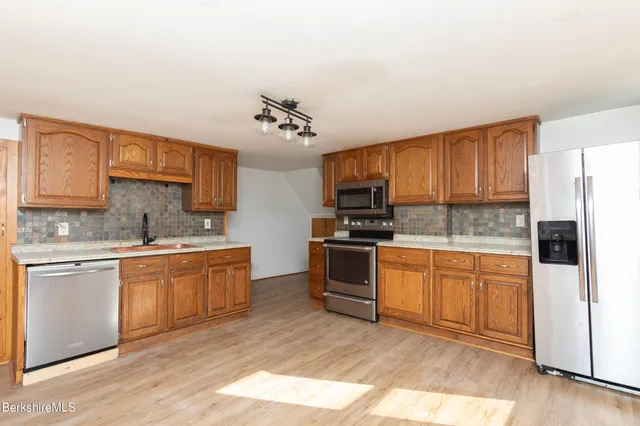 a kitchen with stainless steel appliances granite countertop a stove top oven a sink and dishwasher a refrigerator with wooden floor