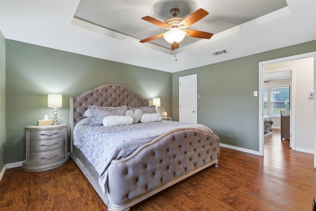 2307 Castle Rock Road Carrollton, TX 75007 - Photo 20 of 34 This bedroom features warm wood flooring, a tray ceiling, and a ceiling fan with light