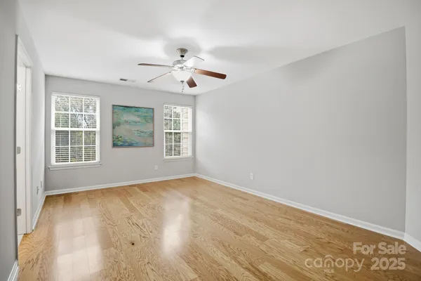an empty room with wooden floor chandelier fan and windows