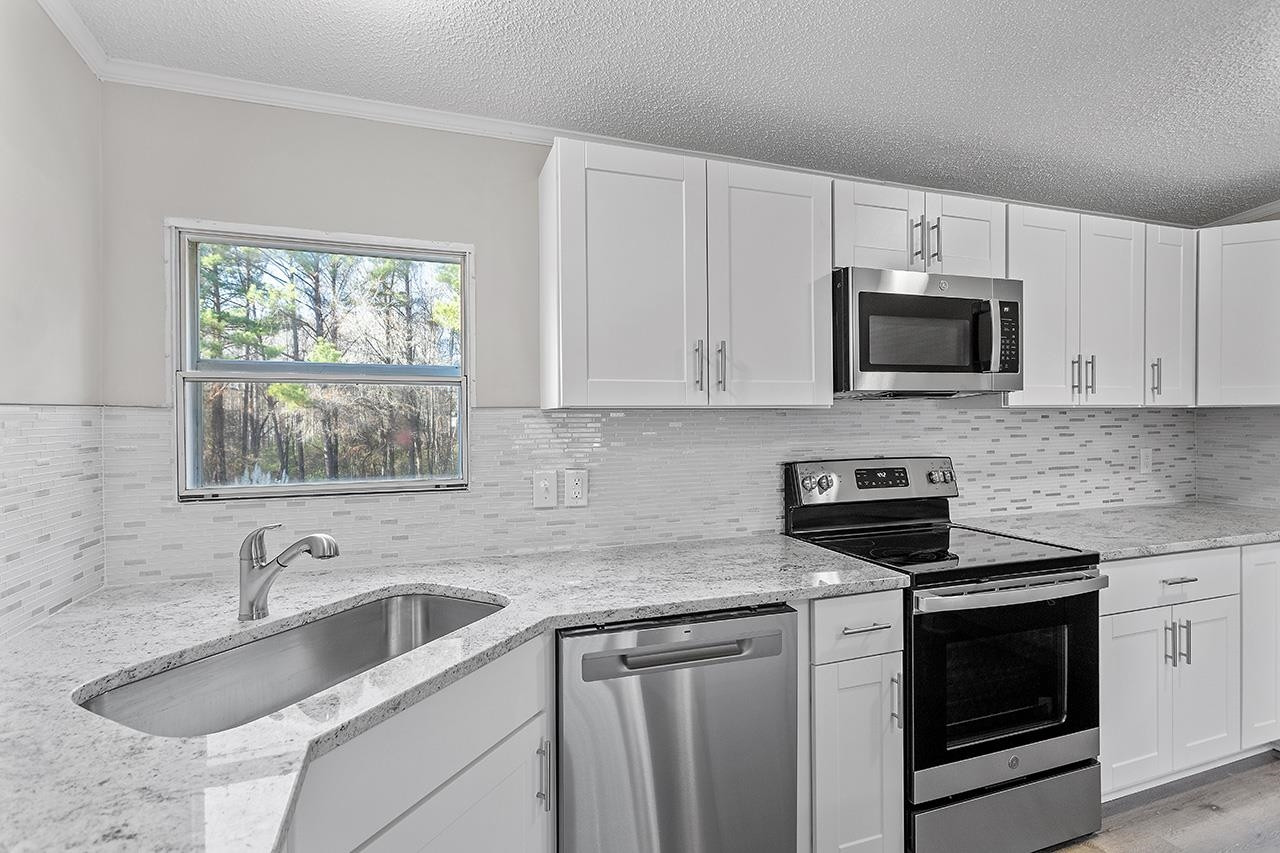 8401 South Creek Road Willow Spring, NC 27592 - Photo 9 of 24 a kitchen with stainless steel appliances granite countertop white cabinets a stove a microwave and a window