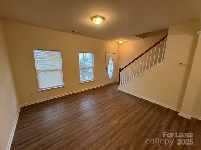 a view of an empty room with wooden floor and stairs