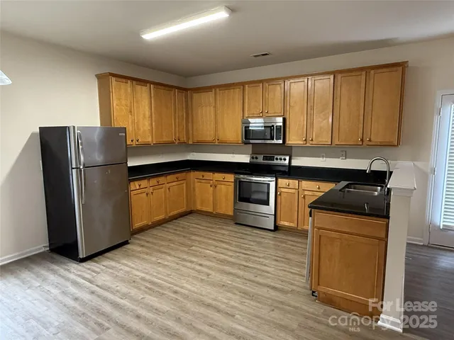 a kitchen with stainless steel appliances granite countertop a refrigerator a sink a stove top oven and wooden floors