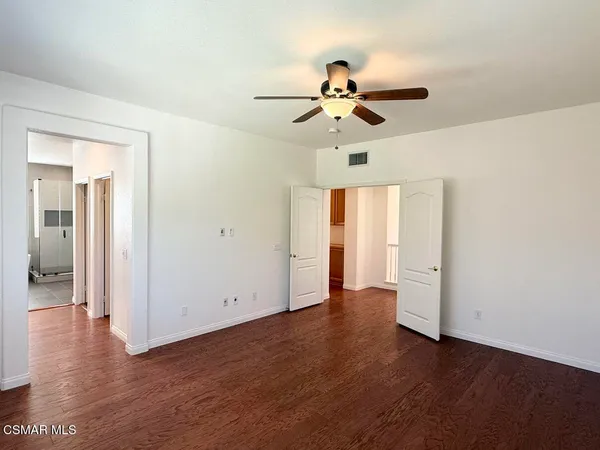 an empty room with wooden floor chandelier fan and windows